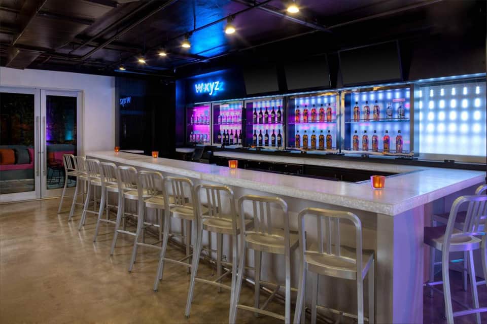 Contemporary bar lounge with blue neon lighting, illuminated bottle displays, and chrome bar seating
