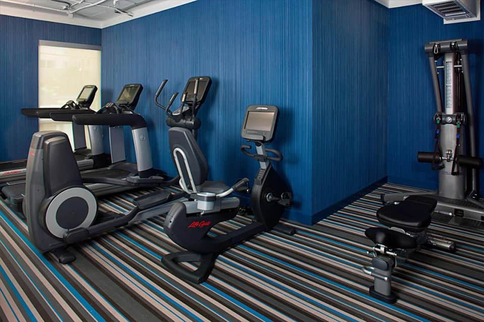 Modern fitness center with blue walls, treadmills, elliptical machines, and exercise bikes