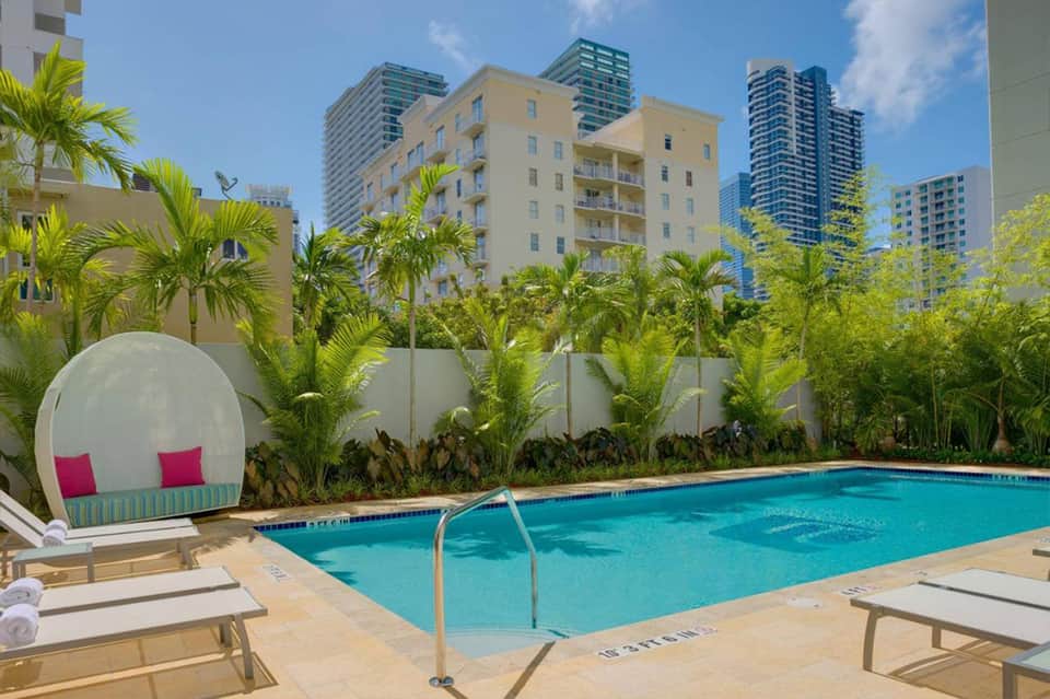 Resort pool with turquoise water, white cabana, palm trees, and high-rise buildings in background