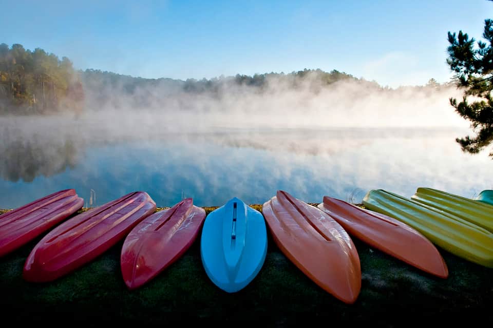 Colorful kayaks lined up on grassy shore overlooking misty lake and forested landscape