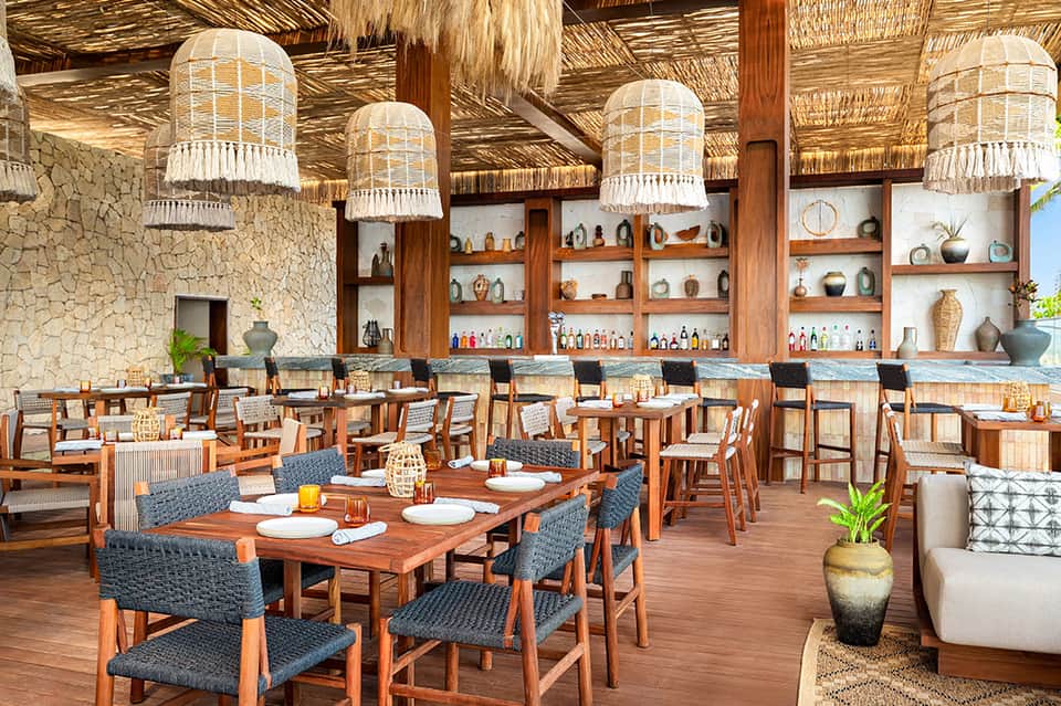 Upscale restaurant with wooden beams, woven pendant lights, decorative shelving, and dining tables