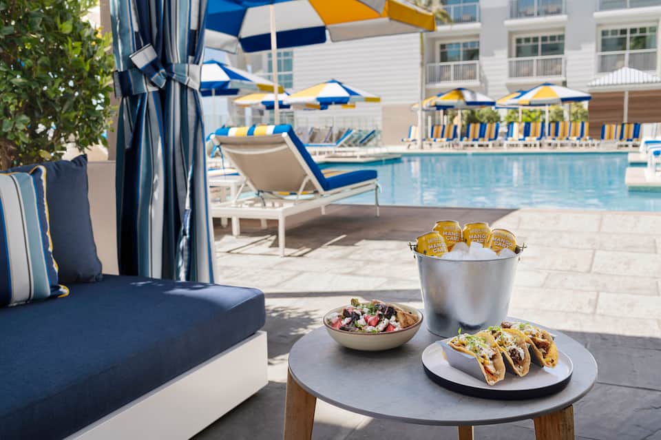 Poolside lounge with tacos, salad, and drinks under blue and yellow umbrellas