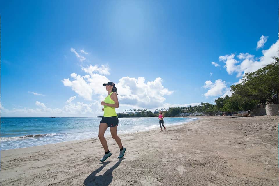 Woman jogging on beach in neon yellow top with ocean and palm trees in background