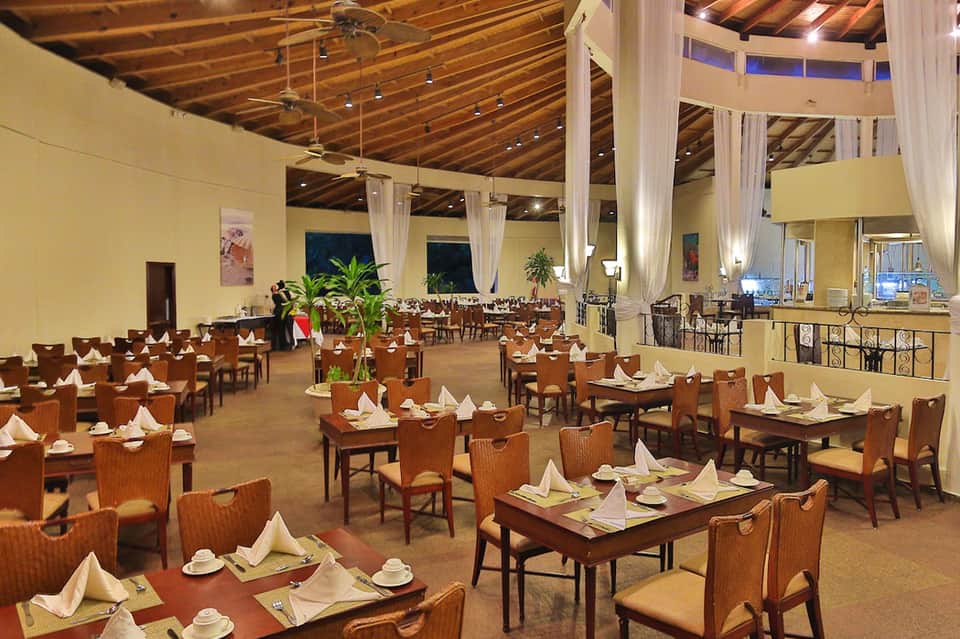 Elegant dining room with wooden chairs, white linens, exposed wooden ceiling, and tall curtains