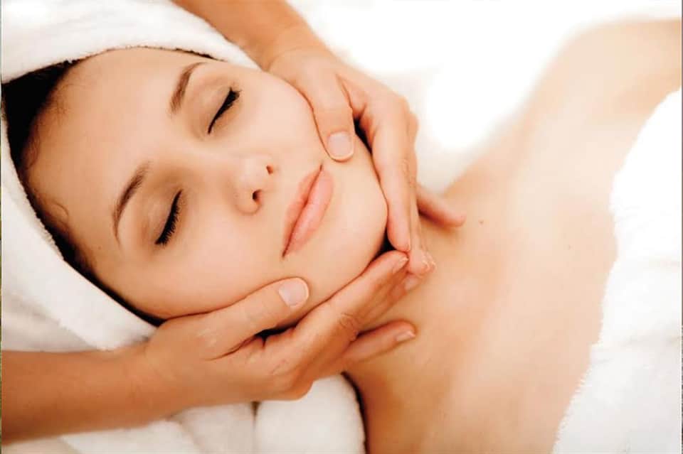 Woman receiving facial massage or spa treatment with eyes closed and white towel headwrap