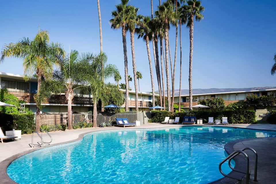 Resort swimming pool surrounded by palm trees with lounge chairs and covered seating areas