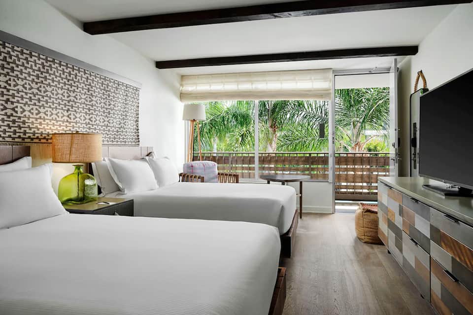 Modern hotel room with two queen beds, balcony with palm trees, and flat-screen TV