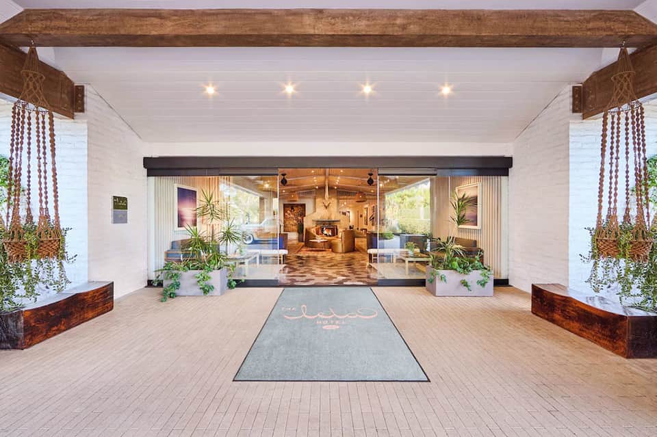 Covered wooden deck entrance with hanging plants, pendant lights, and glass doors to interior lobby