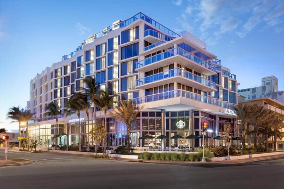 Contemporary multi-story hotel building with blue-tinted glass balconies and ground-level retail storefronts