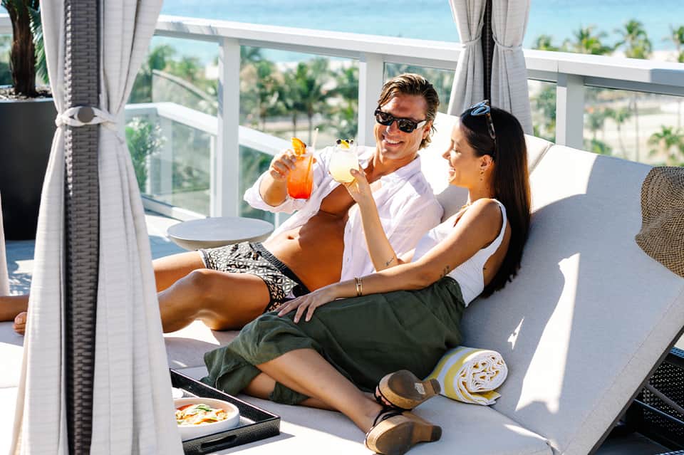 Couple enjoying tropical cocktails on a sunny beachfront terrace with ocean views