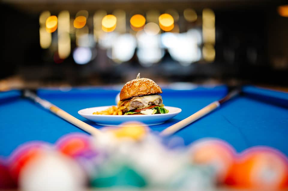 Gourmet burger with fries on a plate at a billiards table with colorful balls