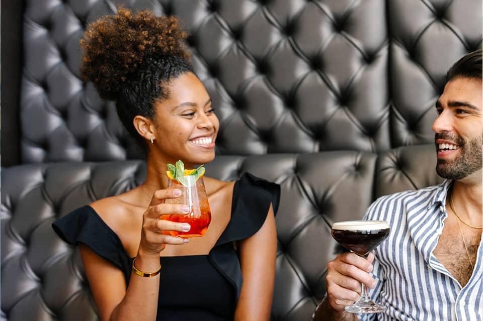 Two people enjoying cocktails on tufted gray seating in an upscale bar
