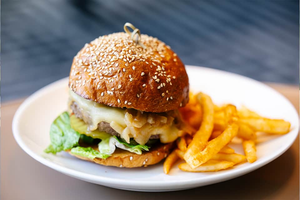 Gourmet burger with sesame seed bun, melted cheese, lettuce, and crispy golden fries on white plate
