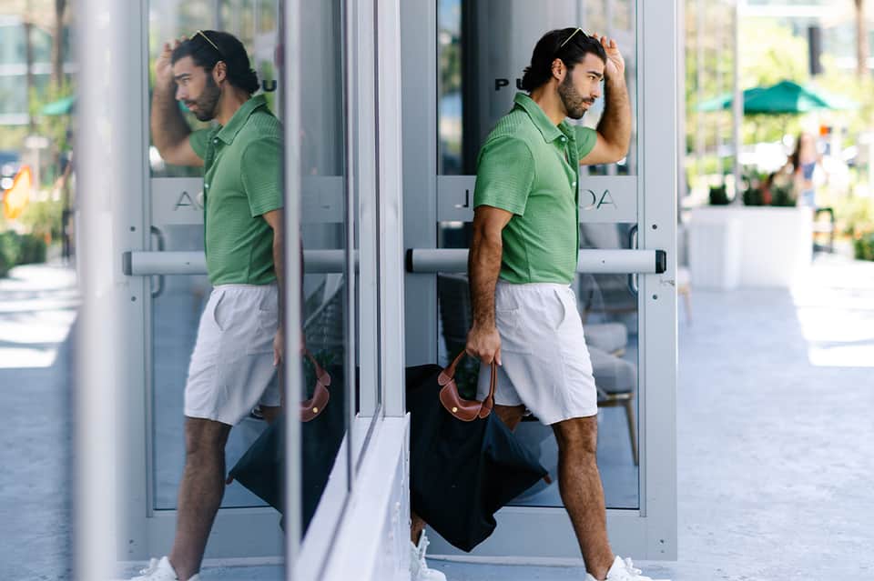 Man in green polo shirt and white shorts entering glass doors of a modern building