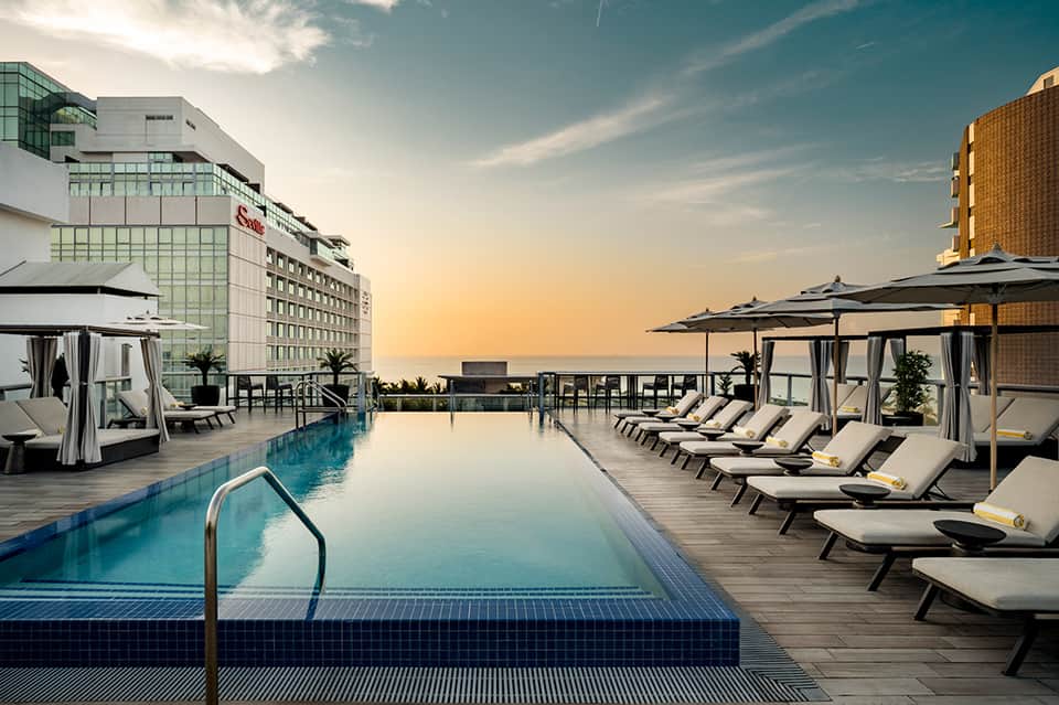 Rooftop infinity pool at sunset with loungers, umbrellas, and city skyline views