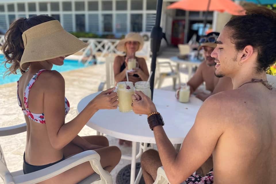 Couple toasting drinks at poolside bar table with umbrellas and lounge chairs