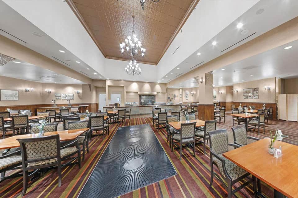 Modern hotel dining room with wood accents, chandeliers, striped carpet, and wooden tables