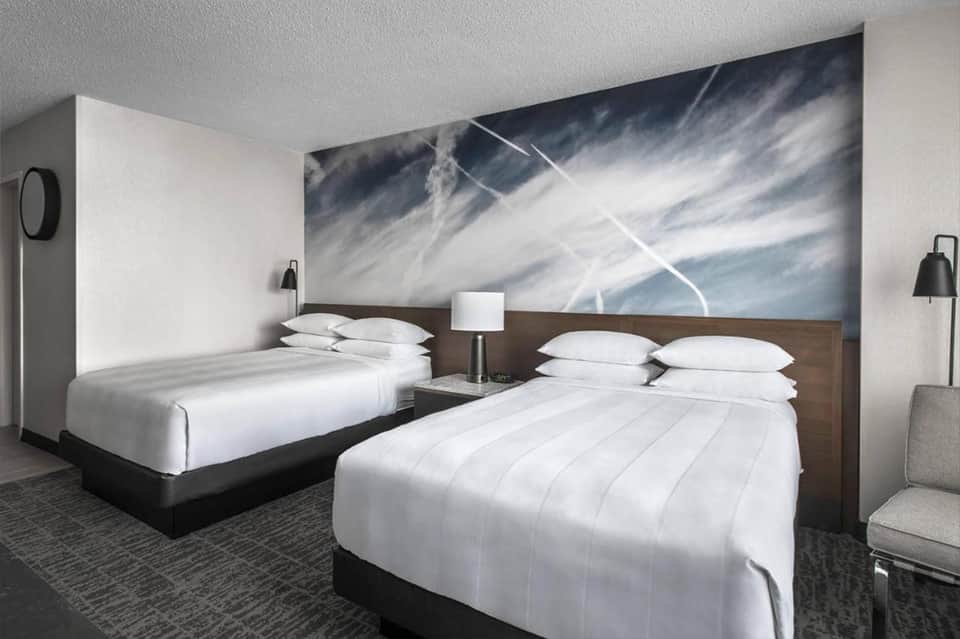 Hotel room with two queen beds, white linens, and abstract sky artwork