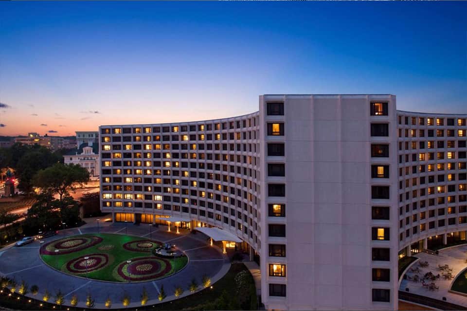 Modern hotel building at dusk with illuminated windows and decorative courtyard gardens