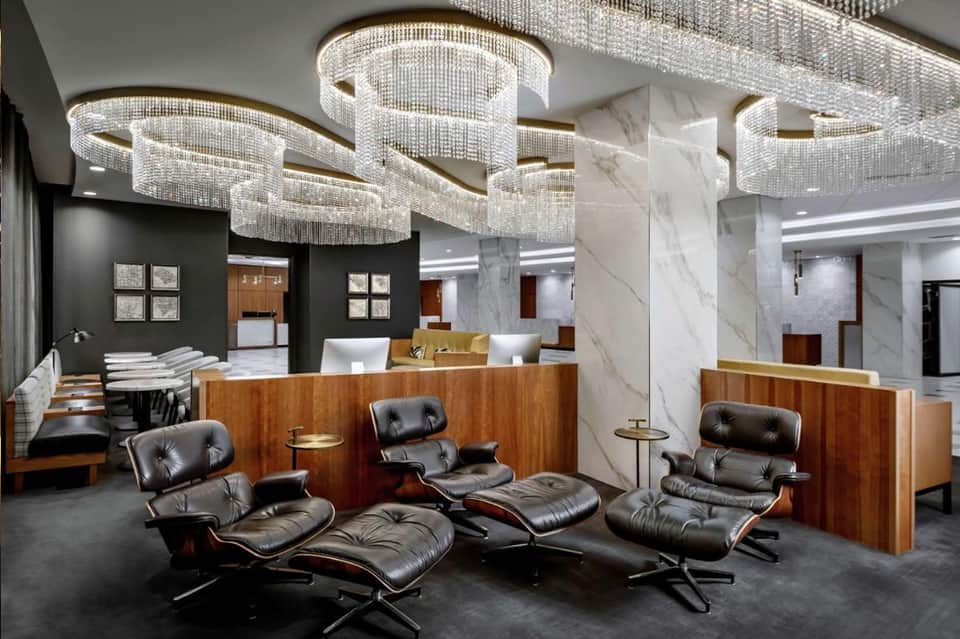 Modern hotel lobby with crystal chandeliers, marble columns, leather chairs, and wood reception desk