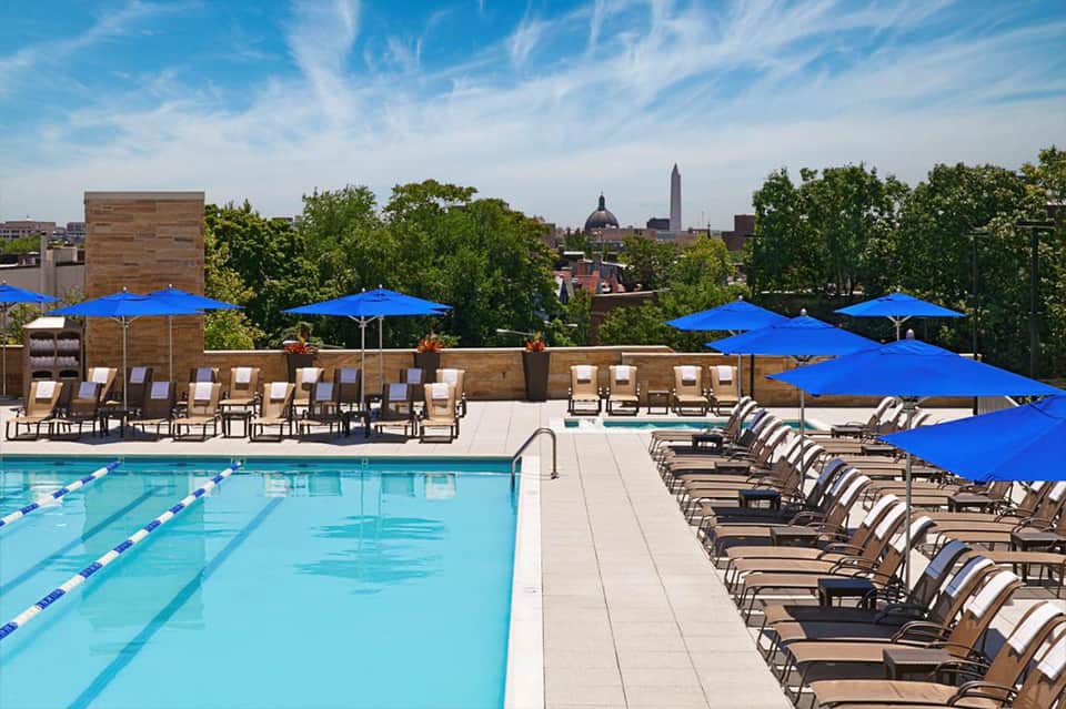 Outdoor swimming pool with lane markings, lounge chairs, and blue umbrellas, Capitol building visible in distance