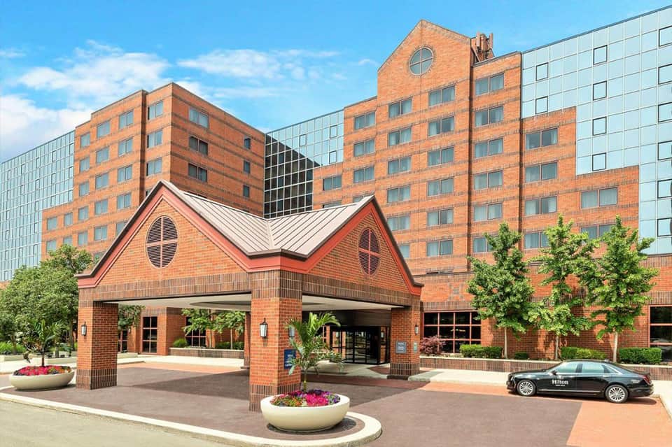 Brick hotel entrance with peaked roof, circular window, and flowering planters