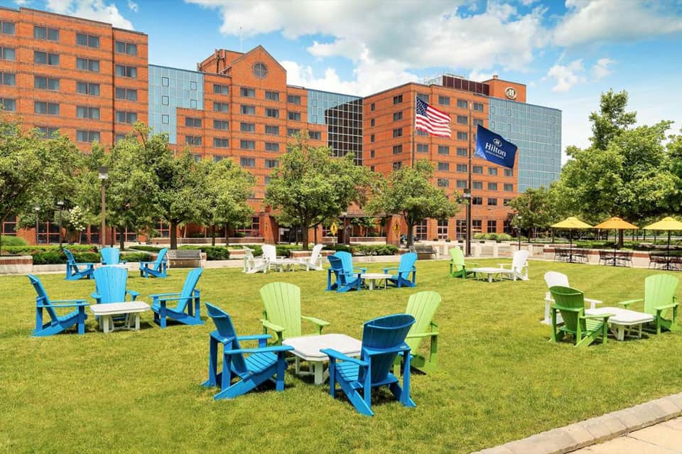 Hotel courtyard with colorful Adirondack chairs on lawn, brick building with American flag visible