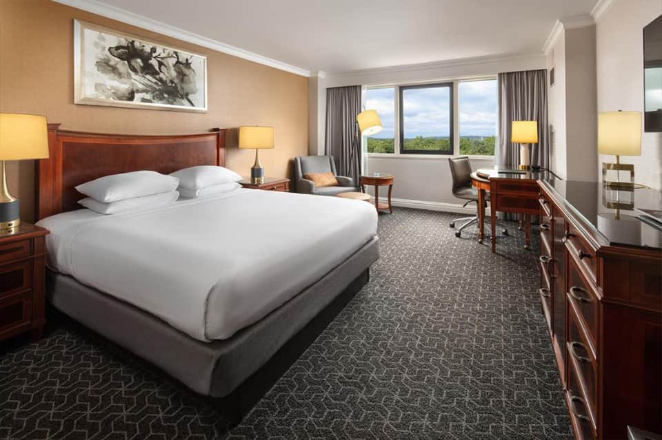 Upscale hotel bedroom with wood furnishings, warm lighting, and panoramic window views