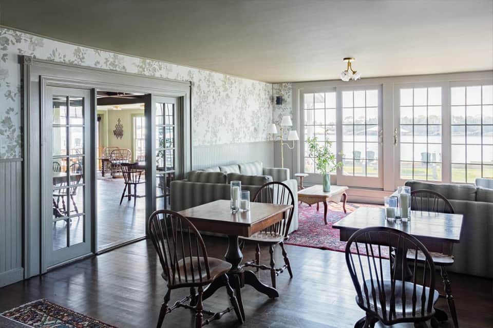 Elegant dining room with fireplace, large windows overlooking water, and classic black Windsor chairs