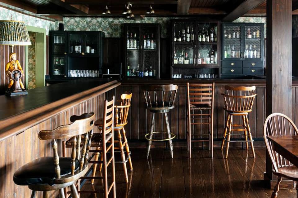 Classic wooden bar with dark cabinetry, glass shelving, and traditional bar seating
