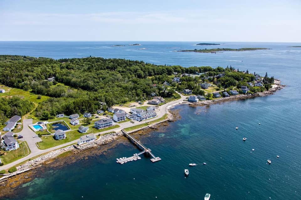 Aerial coastal view of waterfront residential community with dock, boats, and forested peninsula