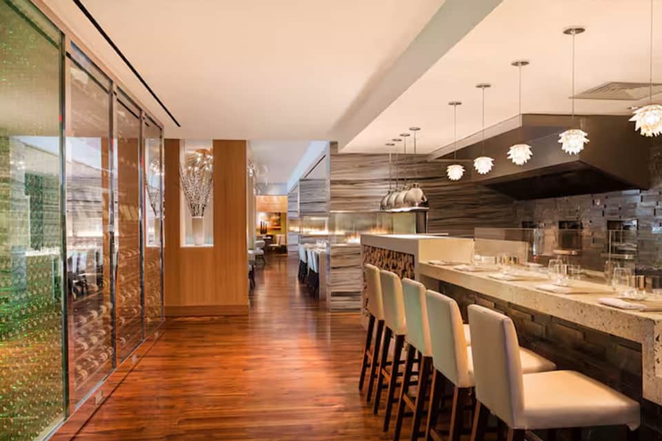 Modern upscale restaurant interior with wooden floors, bar seating, pendant lights, and contemporary design