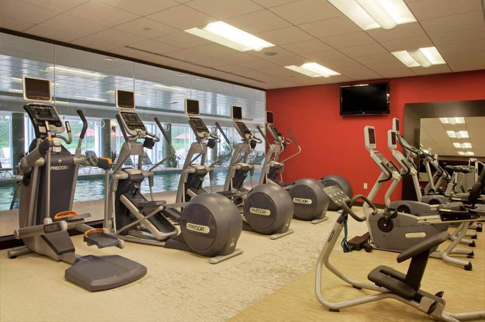 Fitness center with elliptical machines, exercise bikes, and red accent walls