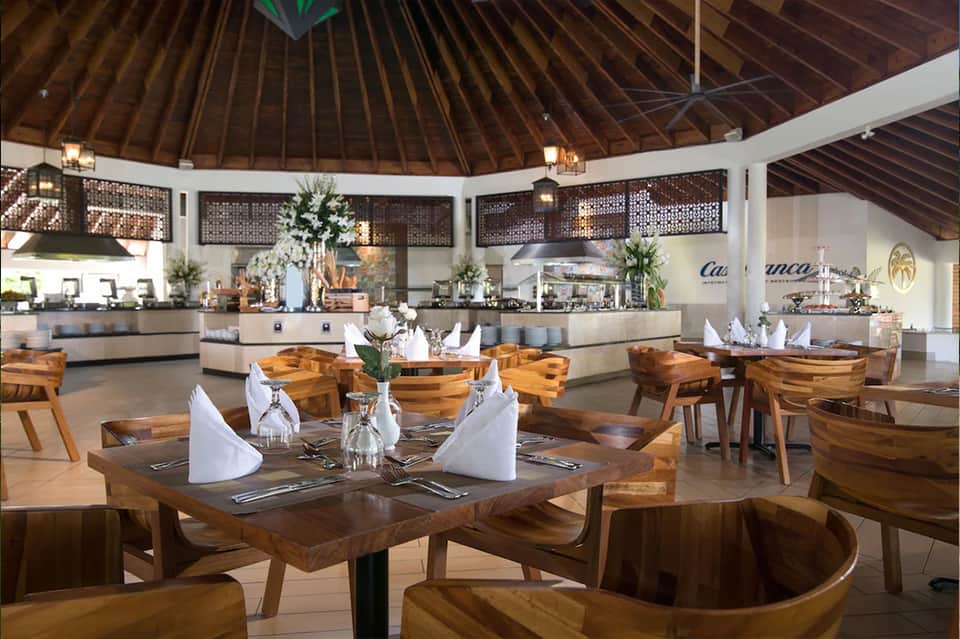 Modern dining room with wooden tables, chairs, and a circular bar under a high wooden ceiling