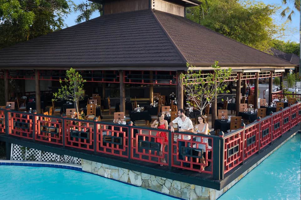 Asian-inspired restaurant pavilion with red geometric railings, dark roof, and waterfront seating area