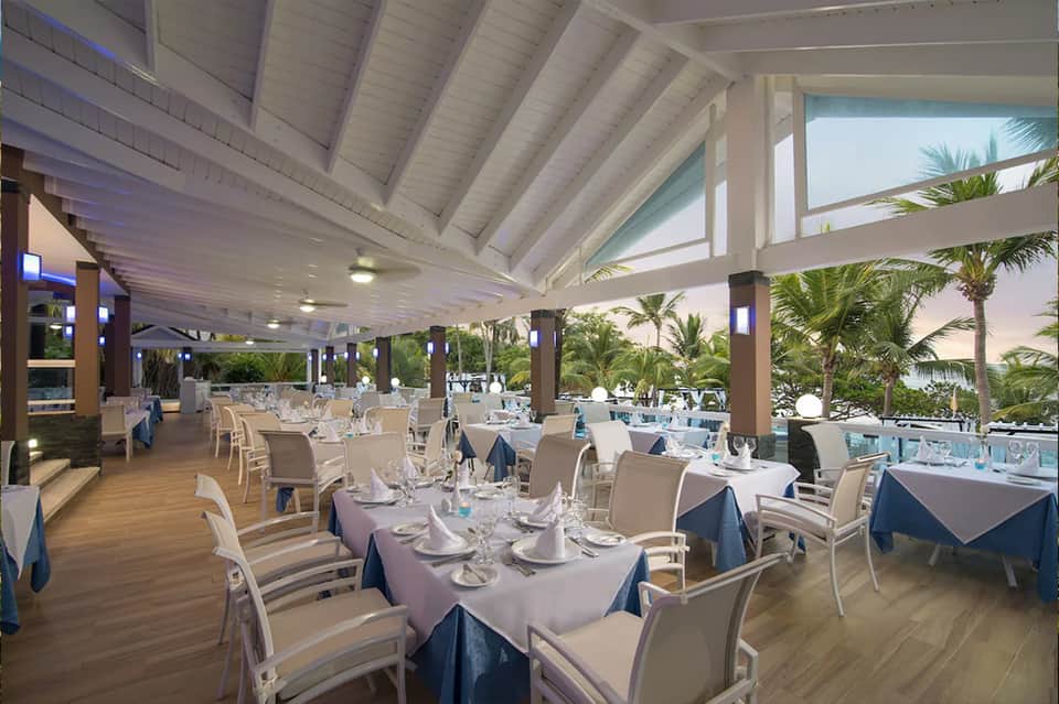 Upscale beachfront restaurant with white columns, palm trees, and ocean views
