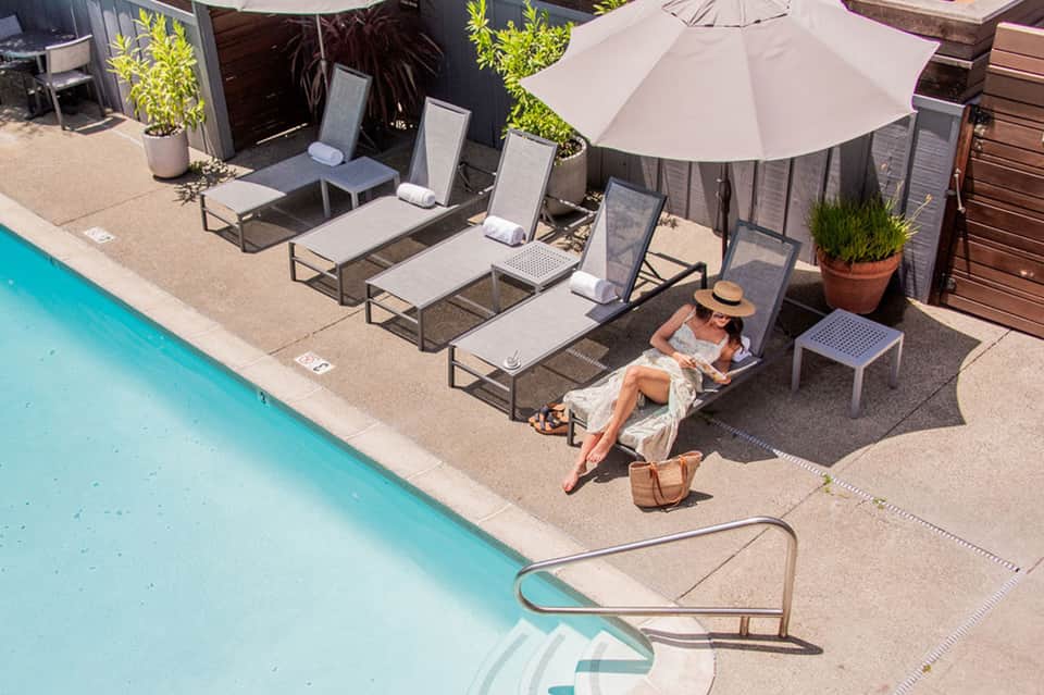 Resort pool area with lounge chairs, white umbrella, guest reading under shade near turquoise water