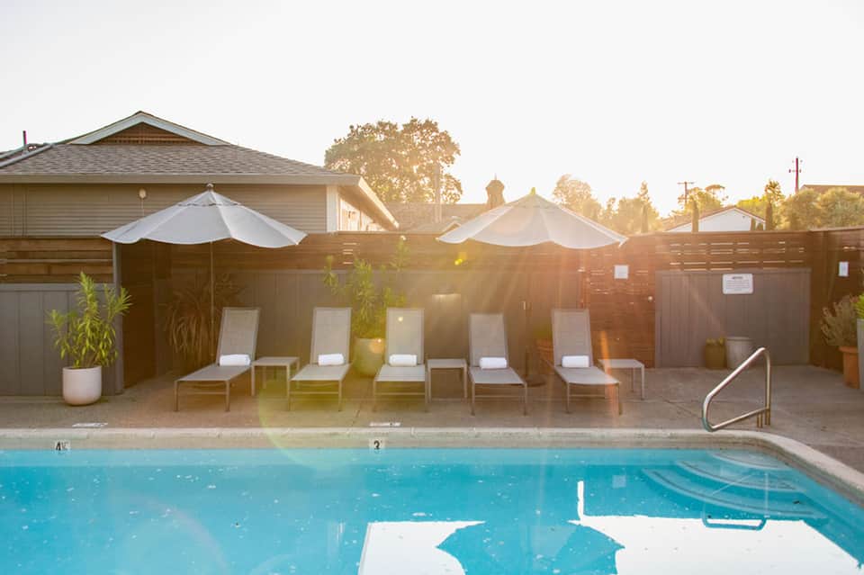 Residential pool deck at sunset with white lounge chairs and umbrellas, brick building backdrop