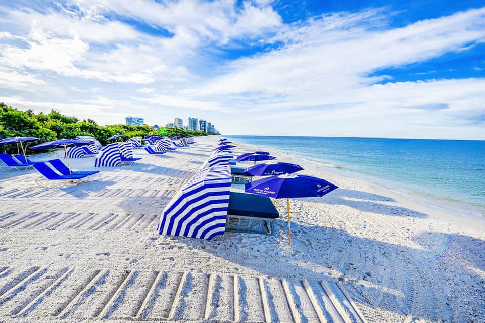 Blue and white striped beach umbrellas and lounge chairs on sandy beach with ocean and city skyline