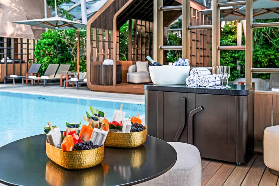 Pool area with modern wooden structures, cocktail service with fresh drinks and appetizers on table