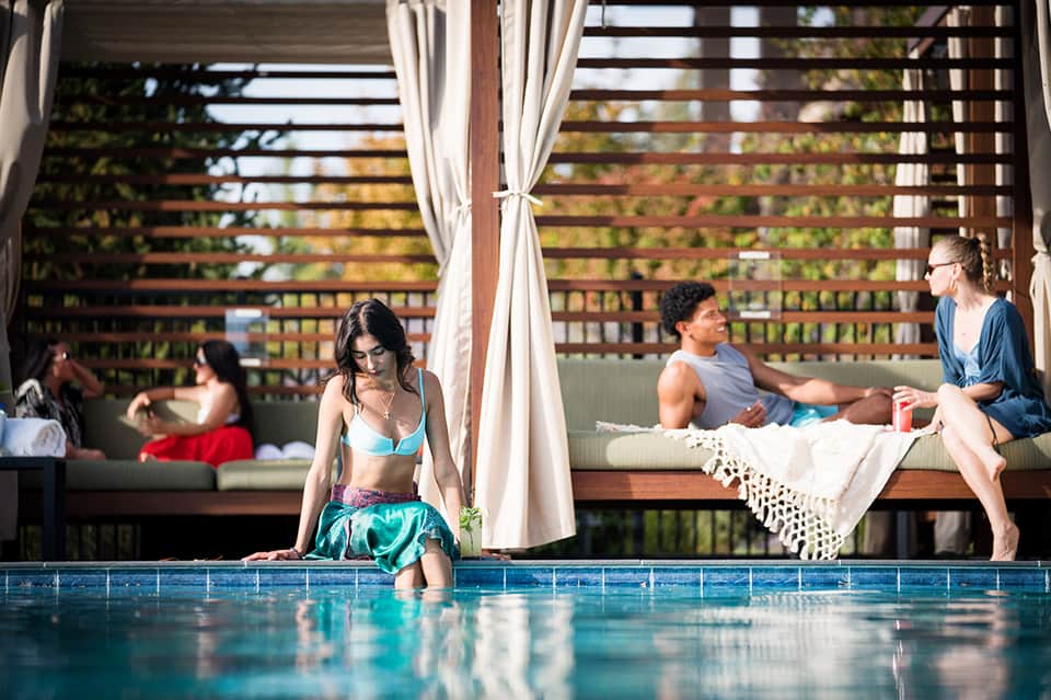 Resort pool with guests relaxing on lounge chairs under pergola with ocean views