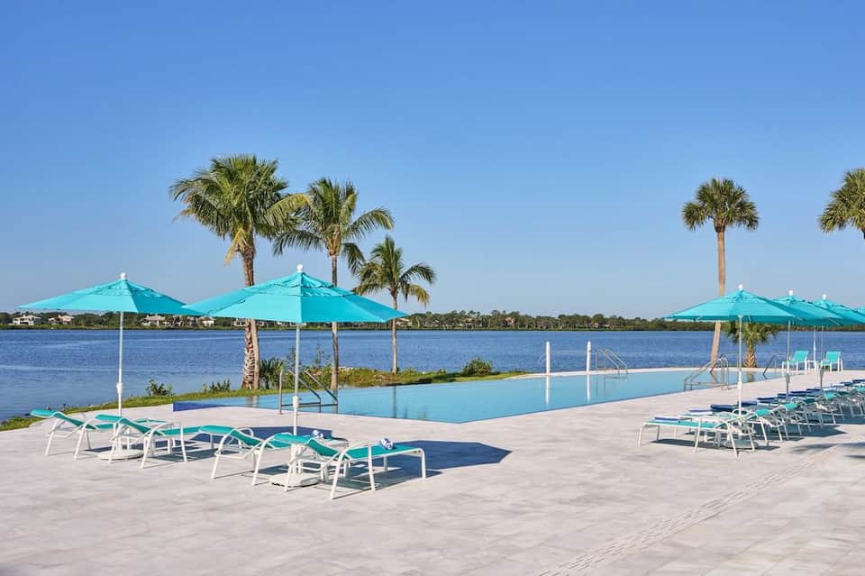 Waterfront pool area with turquoise water, white loungers, turquoise umbrellas, and palm trees by river