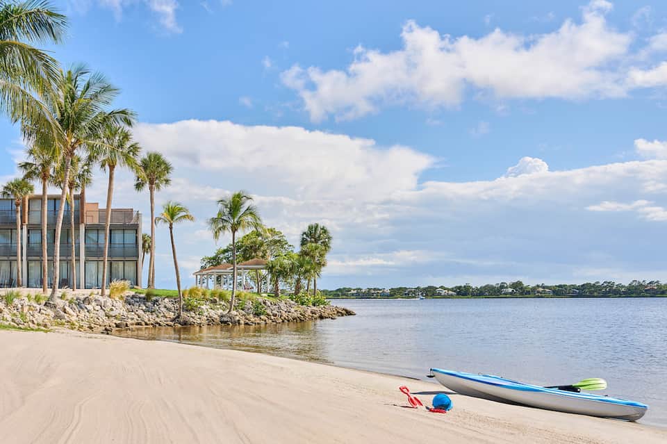 Beachfront resort property with palm trees, sandy beach, kayaks, and calm waterway