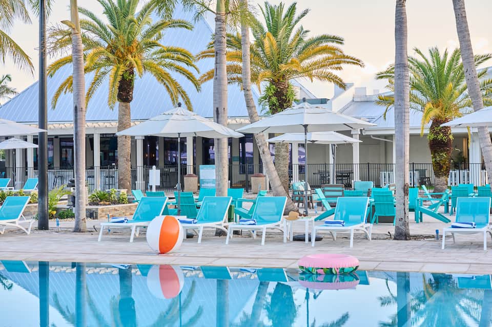 Poolside lounge area with turquoise chairs, white umbrellas, and palm trees
