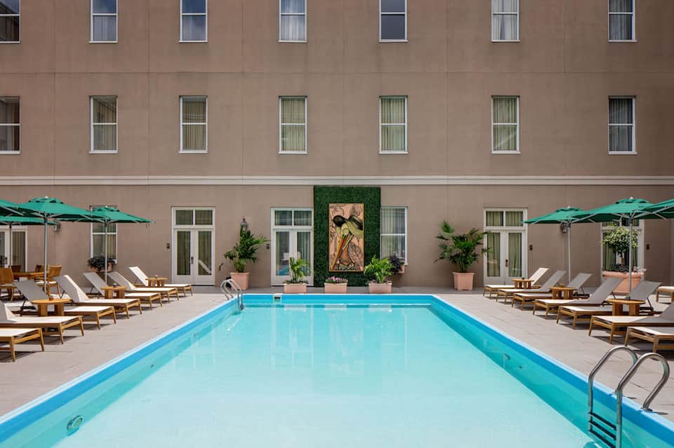 Resort courtyard with turquoise pool, lounge chairs, green umbrellas, and tan building facade