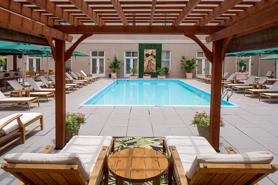 Indoor-outdoor pool surrounded by wooden pergolas, white lounge chairs, and potted plants