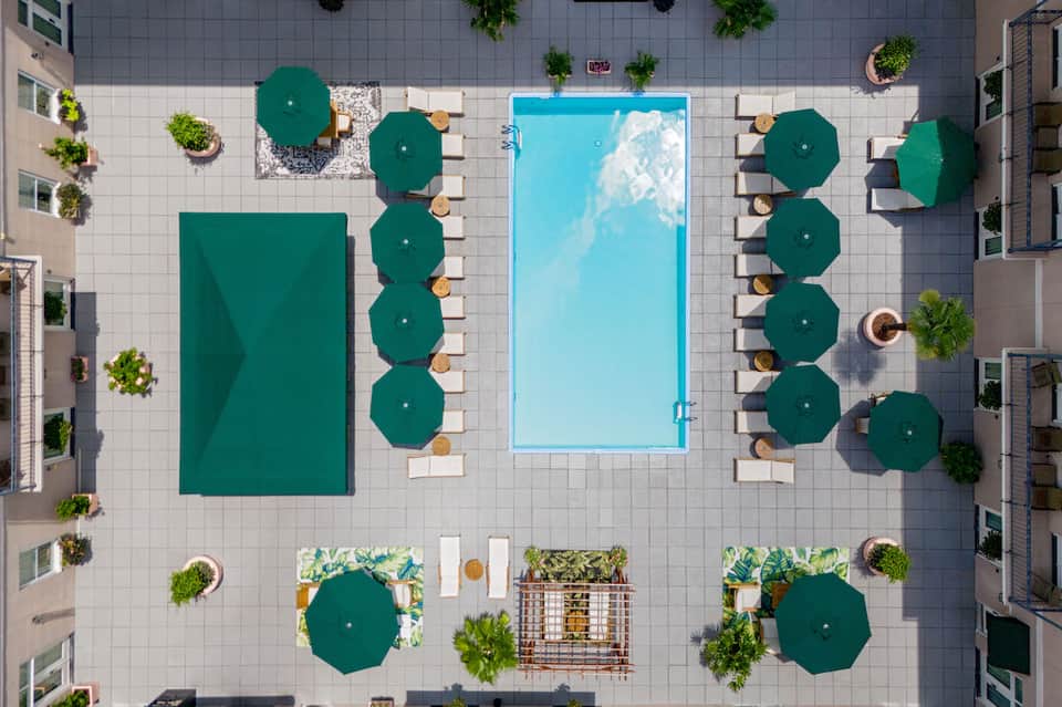 Aerial view of resort pool deck with green umbrellas, loungers, and surrounding tropical vegetation