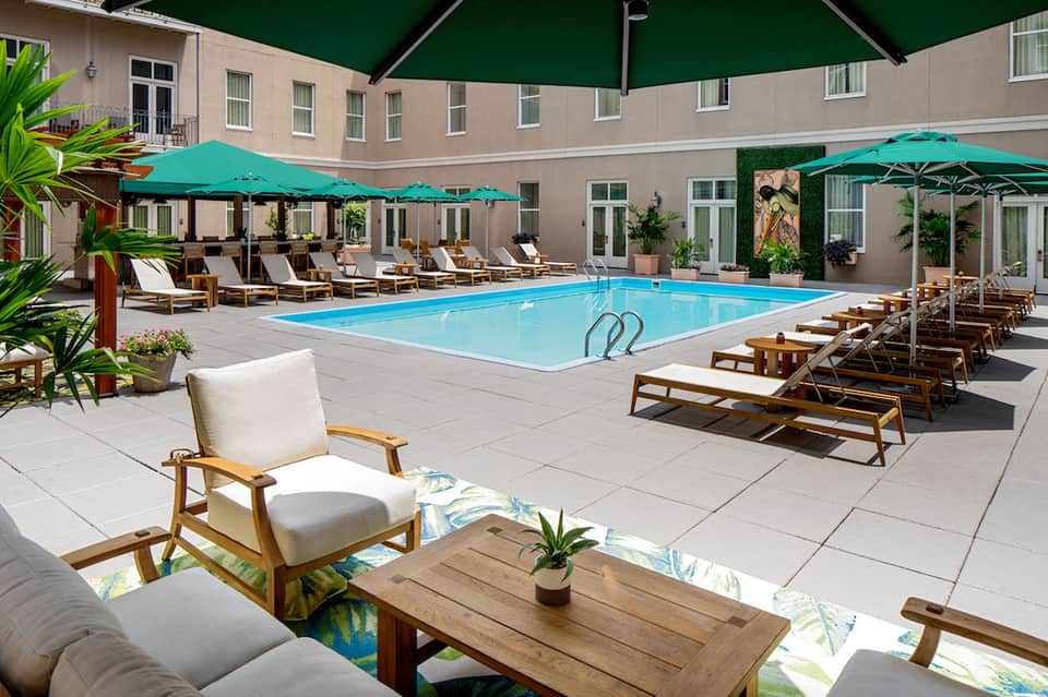 Resort courtyard pool with turquoise water, lounge chairs, and green umbrellas