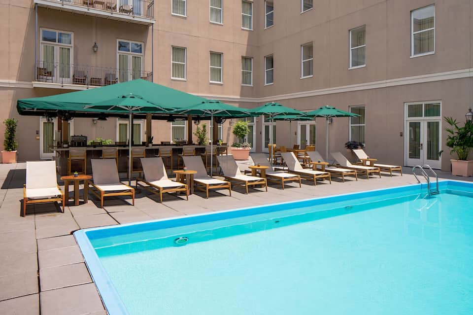 Resort courtyard pool with green umbrellas, wooden lounge chairs, and surrounding hotel building