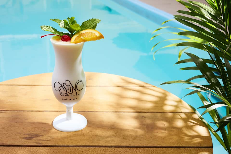 Tropical cocktail in branded glass with orange slice and mint by poolside